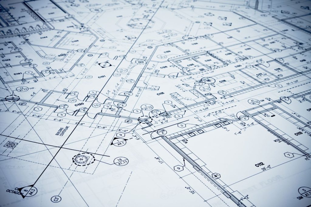 Close-up of detailed architectural or engineering site plans and technical drawings, showing property boundaries, structural layouts, and building annotations on blue-tinted drafting paper.